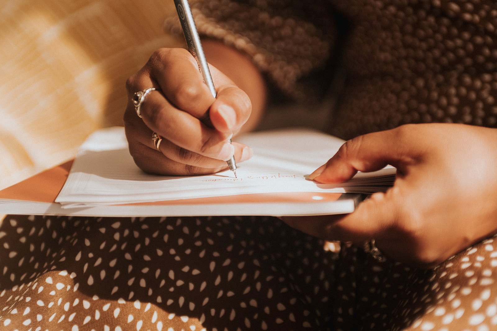 a closeup image of a brown hand holding a pen against a notebook
